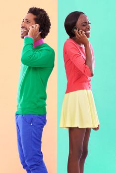 Hipster convo. Studio shot of a young couple using cellphoes standing against a colourful background.