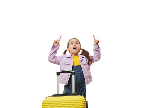 Amazed little traveler expressing wow emotion looking up and pointing forefingers at copy ad space, on white background