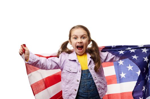 Mischievous funny little girl, American citizen carries US flag, looks at camera, isolated on white background. Ad space