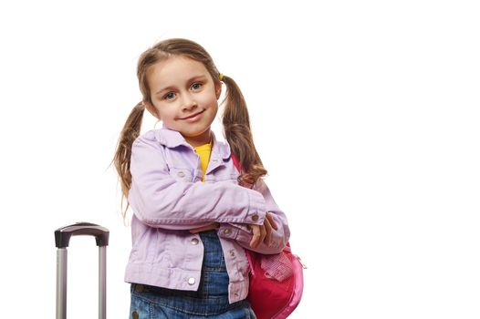 Preschooler lovely little girl with two ponytails, posing with pink backpack and suitcase over white background. Travel