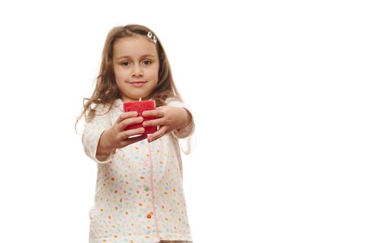 Focus on a red lit candle in the hands of blurred cute little girl in pajamas, smiling at camera over a white background