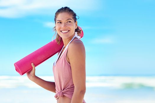 Seaside yoga. a young woman holding a yoga mat while standing on the beach.