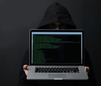 Technology could be your downfall. an unidentifiable computer hacker holding up a laptop against a dark background.