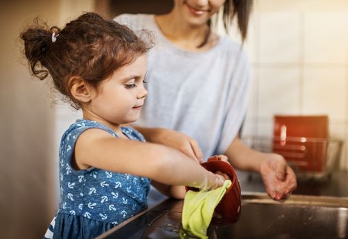 Its a great way to teach them about responsibility. a happy little girl and her mother washing the dishes together at home.