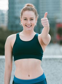 Portrait of one confident young caucasian woman gesturing thumbs up while exercising outdoors. Happy female athlete looking motivated and ready for a good training workout in the city. Endorsing a he