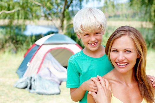 Woman camping with son. Portrait of mother and son camping with tent in background.