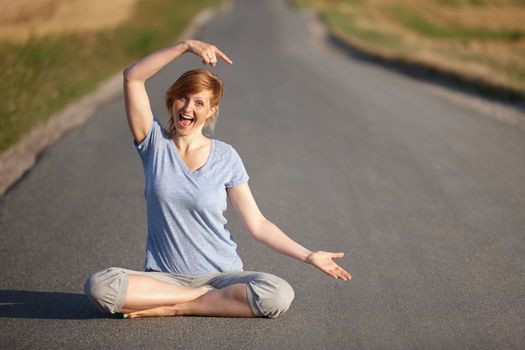 Shes found the road to overall wellbeing. Portrait of a woman looking excited while sitting in the lotus position on a country road.