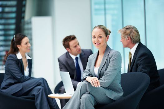 Smiling female executive with business people. Portrait of pretty female executive smiling with business people discussing in background.