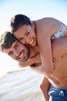 Happiness is the foundation of our love. a young man giving his girlfriend a piggyback on the beach.