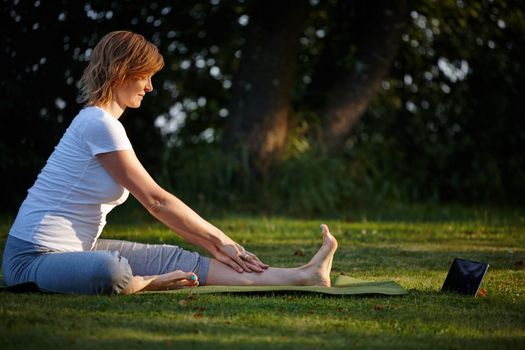 Step-by-step online yoga instructions. an attractive woman doing yoga at the park with her tablet beside her.