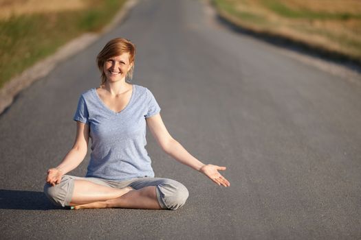 The journey to overall wellbeing. Portrait of an attractive woman sitting in the lotus position on a country road.
