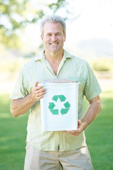 Ensuring a green future for my children. A man standing in a park holding a recycling bin while smiling at the camera.