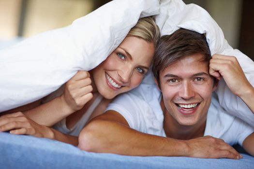 Wrapped in romance. a happy young couple enjoying a playful moment underneath the duvet.