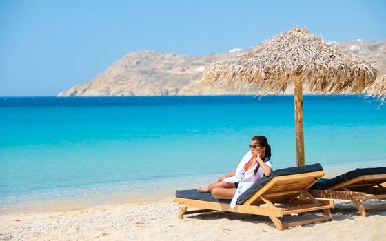 women at Mykonos beach with umbrella and luxury beach chairs at Elia beach Mykonos greece