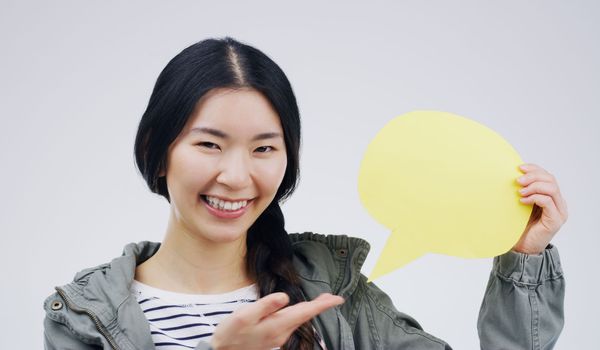 This answers everyones question. Portrait of an attractive young woman holding a speech bubble against a grey background.
