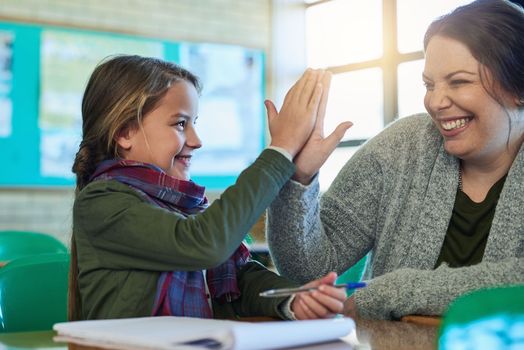 Becoming a top student with the help of her teacher. an elementary school girl high fiving her teacher in class.