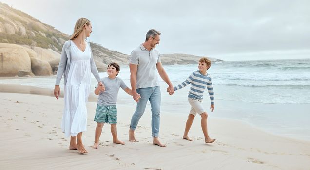 Happy caucasian parents and kids holding hands while walking together along the beach shore during a relaxing fun family summer vacation. Loving mom and dad enjoying leisurely stroll while bonding wi