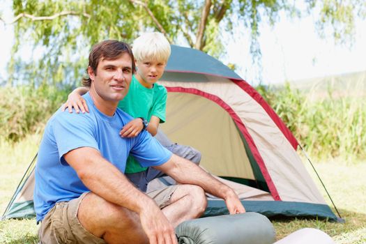 Father and son camping. Portrait of father and son sitting in front of tent
