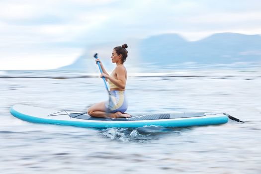 Paddle board, sea and fitness with a sports woman floating on water in nature for wellness or exercise. Earth, training and travel with a female athlete on a paddleboard while on vacation for travel