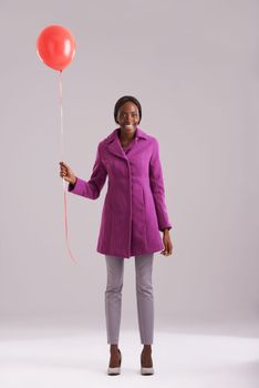 Its the simple things that make me smile. Studio shot of a young woman holding a single red balloon.