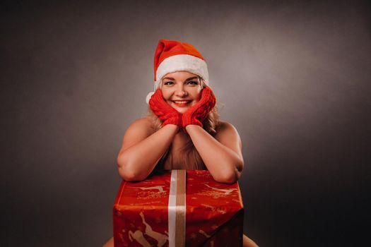 undressed girl in a Christmas hat sits with a gift in a black background