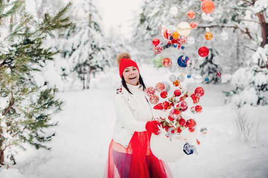 A girl in a white jacket throws Christmas balls to decorate the Christmas tree.A girl throws Christmas decorations from a basket into the winter forest