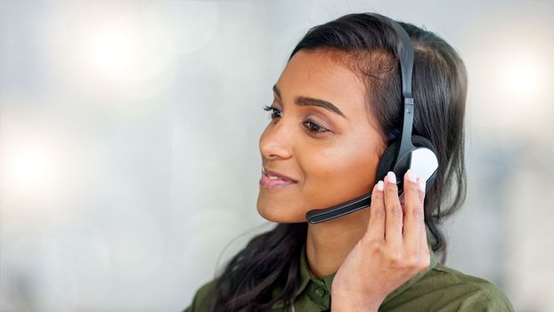 Happy female customer service agent smiling while working in a call centre and talking to a client with a headset. A helpful saleswoman assisting customers with purchase orders and questions online