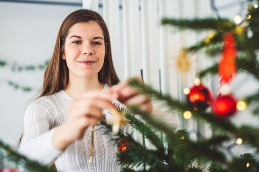 Smiling caucasian woman decorating the Christmas tree putting on the ornaments