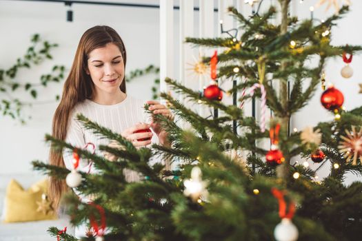 Woman decorating the Christmas tree with festive red ornaments