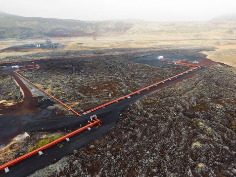 Geothermal power plant pipes, in bright red color standing out from black volcanic soil on the ground