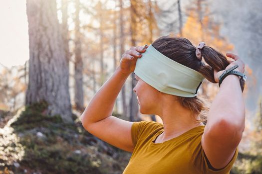 Woman hiker fixing up her headband in the forest while on an autumn hike 