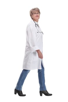 Full length profile studio shot of mature woman doctor in white coat and glasses walking