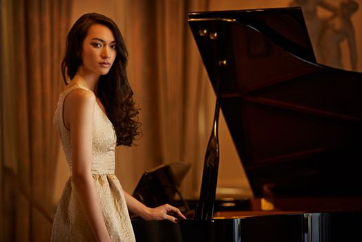 Sophisticated beauty. Portrait of a beautiful young woman posing beside a piano.