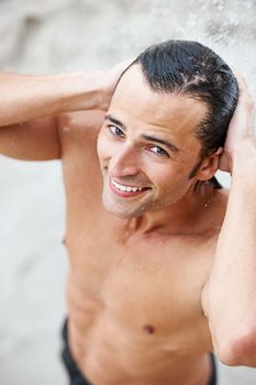 Theres something refreshing about his smile. Portrait of a happy young man smiling while taking a shower outdoors.