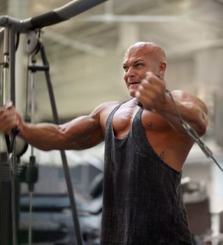 Pushing through the pain. A male bodybuilder using exercise equipment to train at the gym.