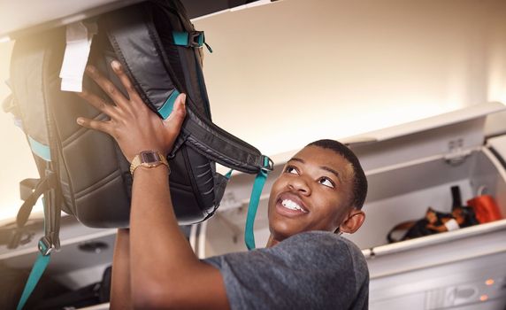 Securing my luggage. a handsome young man putting his luggage in the overhead compartment on an airplane.