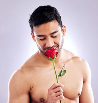 Smells good but I smell better. Studio shot of a handsome young man posing with a red rose.