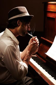 Moody musician. Profile of a handsome man having a smoke at his piano.