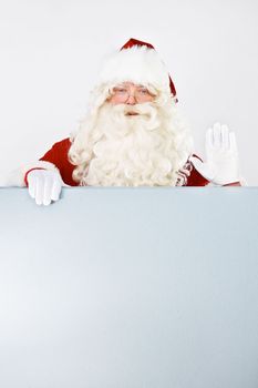 Promoting your christmas message. Portrait of Father Christmas waving with a blank placard - copyspace.