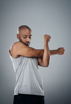 Warm up and do you times ten. a sporty young man stretching against a grey background.