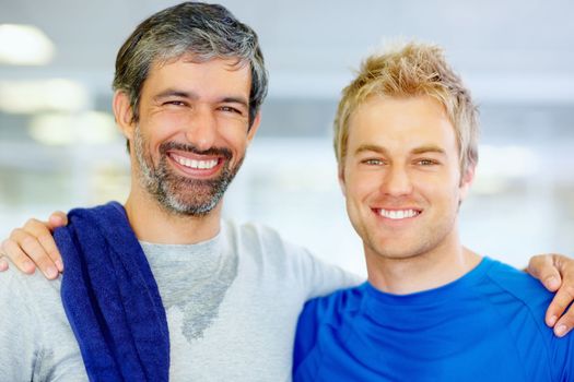 Happy close friends at fitness center. Portrait of two male friends with arms around at fitness center.