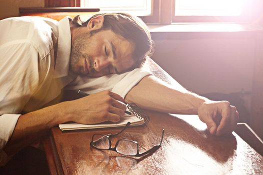 Overworked and underpaid. A handsome young man sleeping on his notebook at a bar.
