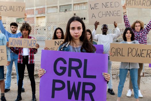 Young woman holding a girl power sign in demonstration for equality and woman's rights. Protesters in the background.