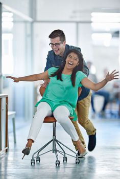 This office is a blast to work in. a male coworker pushing his female coworker around an office in a chair.