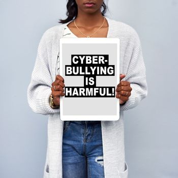 Studio shot of an unrecognizable young woman holding a tablet with the message CYBERBULLYING IS HARMFUL on the screen against a grey background