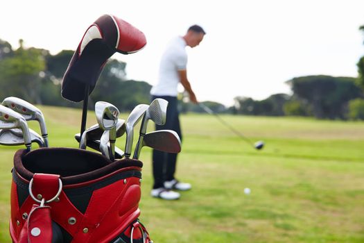 Have gear, will golf. a bag of clubs with a man playing golf in the background.