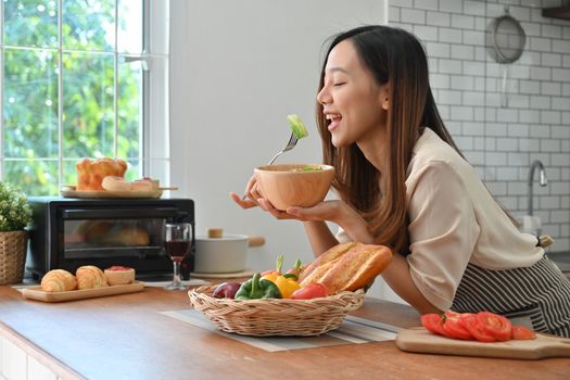 Beautiful woman eating healthy salad in modern kitchen interior. Wellbeing and healthy lifestyle concept.