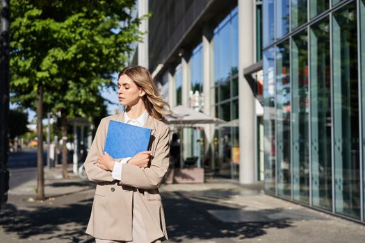 Work and corporate people. Confident businesswoman holding a blue folder with business documents, walking on street