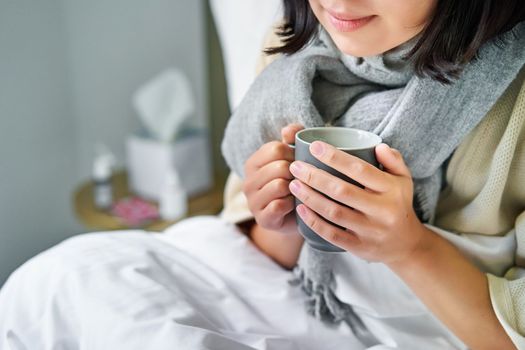 Close up of female hands holding hot drink, lying in bed, girl catching a cold and staying at home