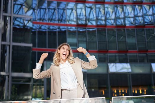 Happy businesswoman dancing on street, raising hands up. Corporate woman celebrates her victory or success